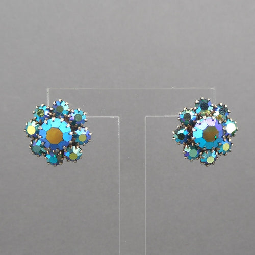 This is a circa 1950 pair of screw back earrings . Cluster style, flower design, dark blue green aurora borealis iridescent rhinestones.  Each approximately 5/8